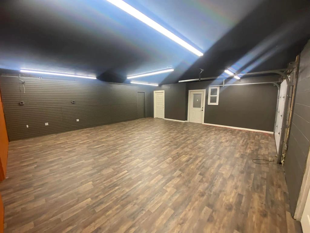 Empty room with gray walls and wood-style flooring, painted by a reputable painting company in Pittsburgh PA, featuring overhead fluorescent lights and a white door.