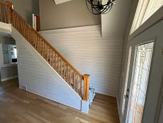 An interior view of a home in Pittsburgh, PA showing a wooden staircase with a white handrail leading upstairs, a chandelier above, and a glass-paneled door on the right.