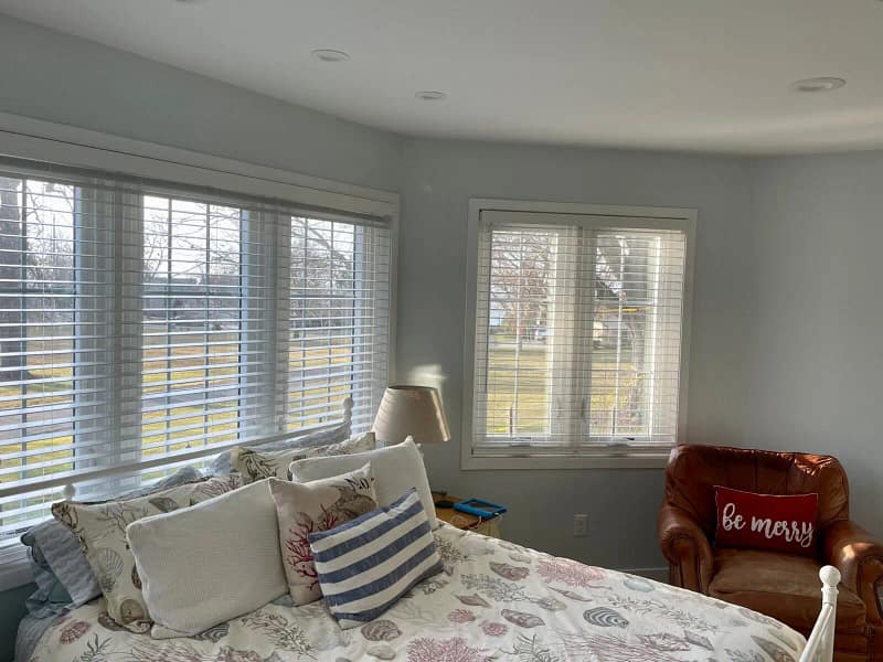 Bright, cozy bedroom with a made bed featuring floral sheets and pillows, a leather armchair near a window recently enhanced by painters in Pittsburgh PA, and a floor lamp.